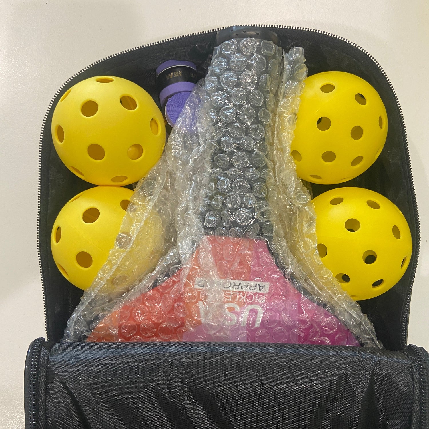 Yellow pickleball balls in a black bag with bubble wrap and pink packaging.